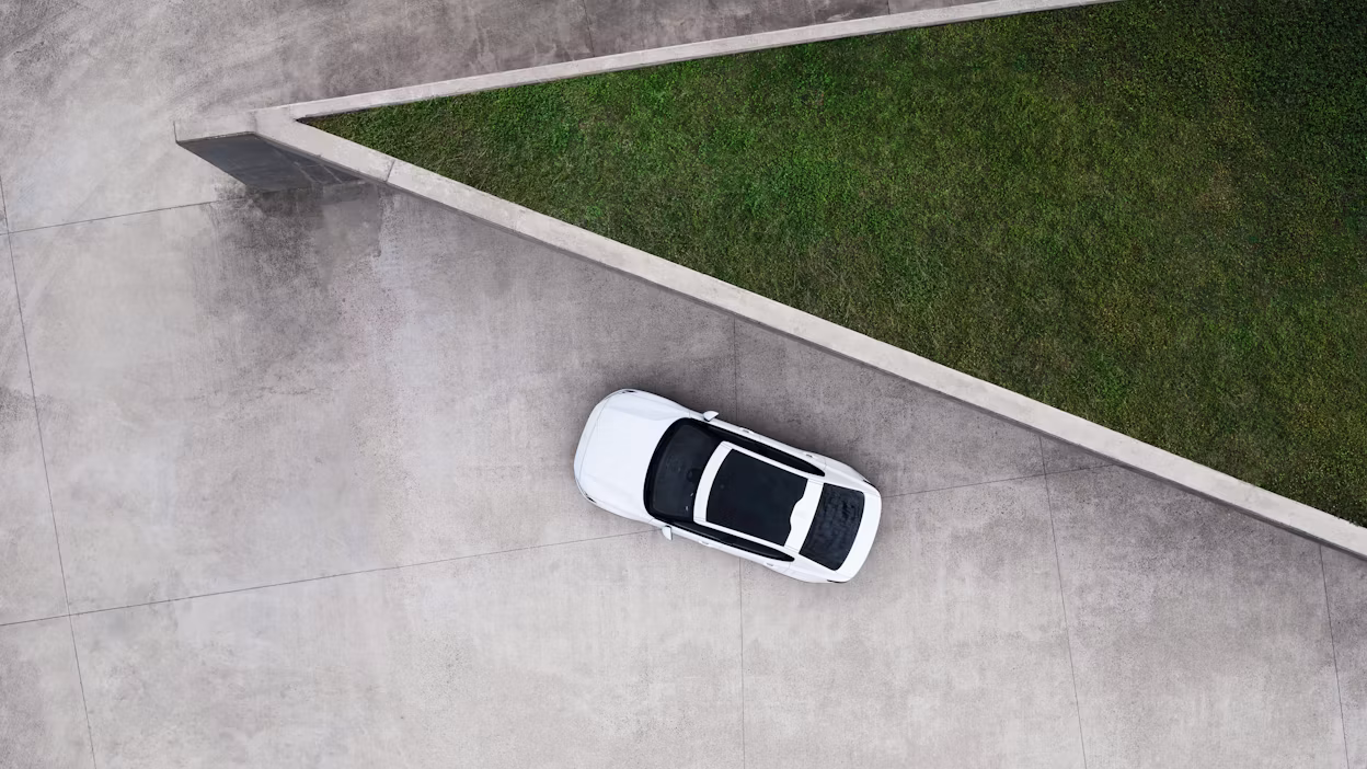 A white Polestar 2 with panoramic roof parked on a concrete platform outside a triangular building with a grass roof.