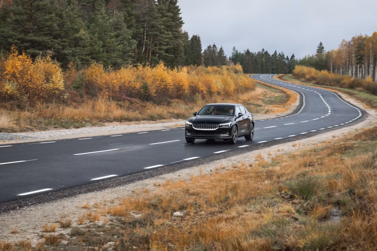 Black Polestar 2 prototype on a forest road in autumn.