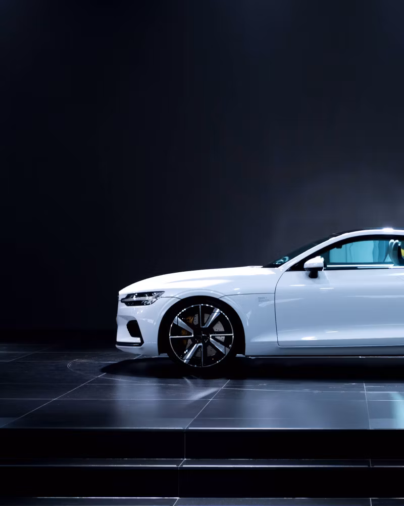 Side view of a white Polestar car on a black platform with dark background.