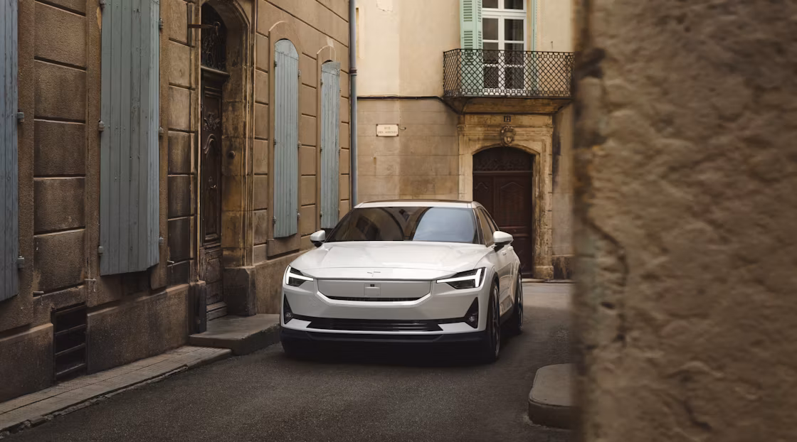 Polestar 2 in Snow colour parked in an alleyway between brown coloured buildings with blue accents.