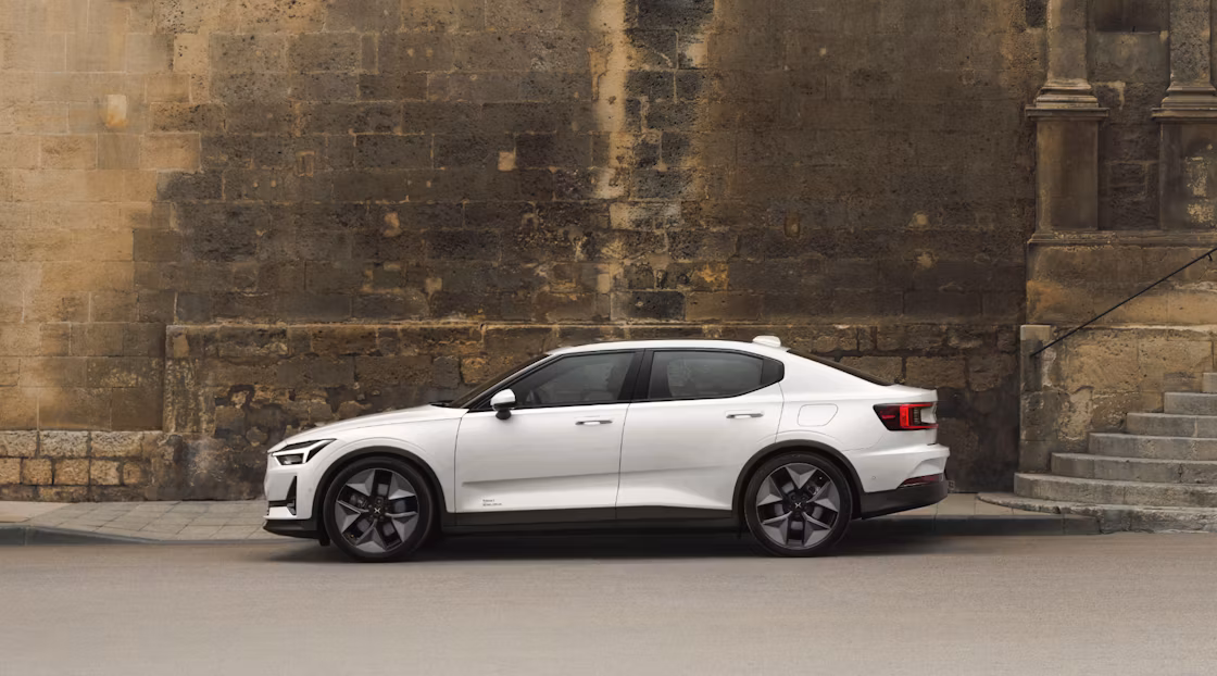 Polestar 2 facing left and standing near a dirty brown brick wall near the sidewalk and some stairs.