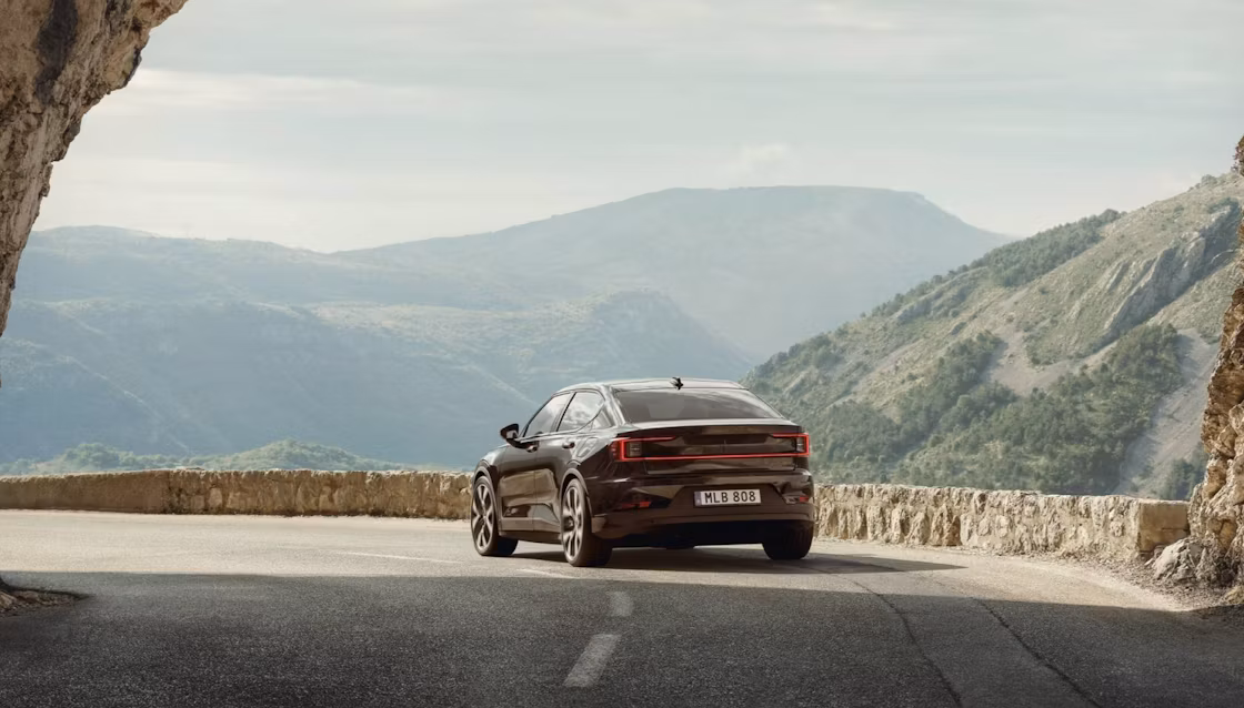 Polestar 2 driving away from an arched rock formation on a highway in a hilly area.