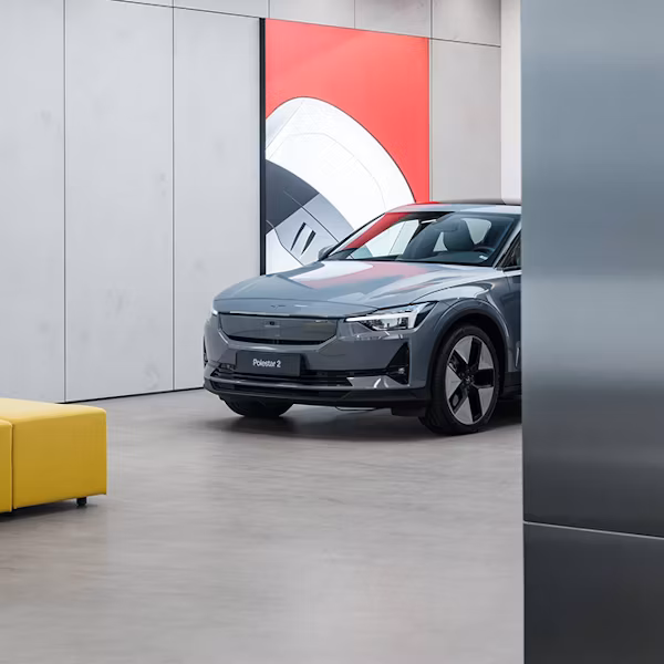 Polestar 2 car parked indoors in a Space near a yellow sofa and a wall with red and white artwork.