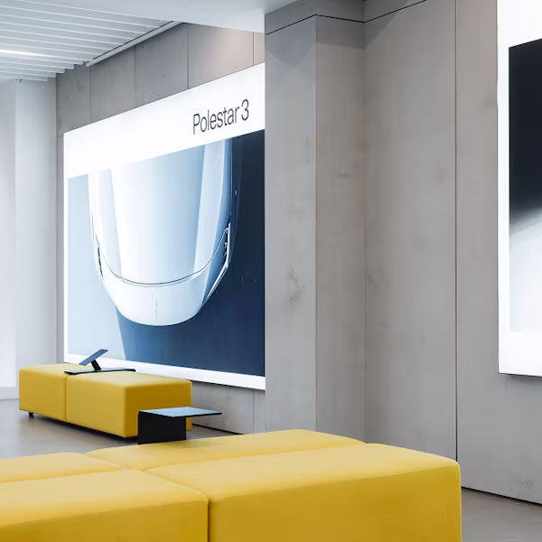 Interior with yellow seating, wall display showing front view of Polestar 3 car.