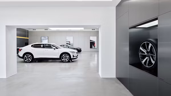White Polestar 2 car in showroom with another car in background and a wheel displayed in a wall compartment.